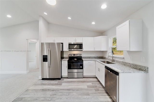 kitchen featuring appliances with stainless steel finishes, light stone counters, sink, white cabinets, and lofted ceiling