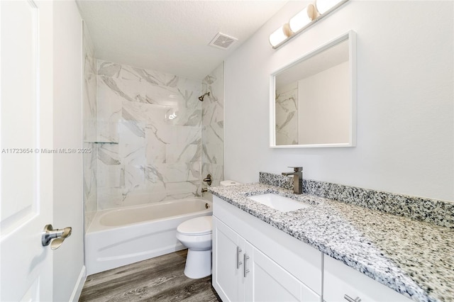 full bathroom with tiled shower / bath combo, a textured ceiling, toilet, vanity, and hardwood / wood-style flooring