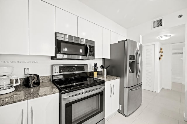 kitchen featuring appliances with stainless steel finishes, light tile patterned floors, white cabinetry, and dark stone countertops