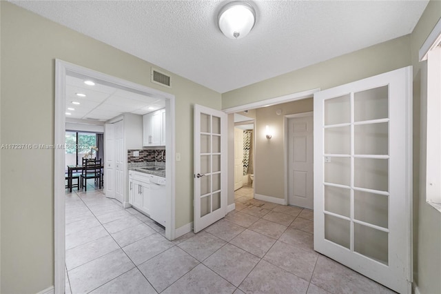 hall with light tile patterned floors, a textured ceiling, and french doors