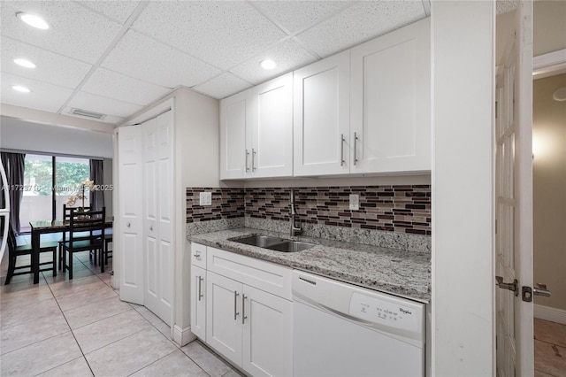 kitchen featuring light stone counters, a drop ceiling, white dishwasher, sink, and white cabinetry