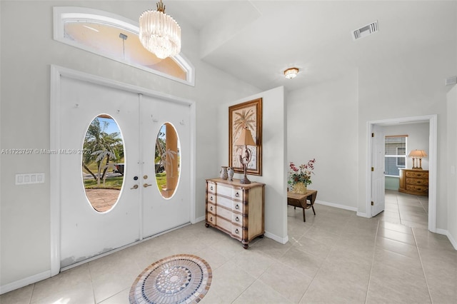 entrance foyer featuring a towering ceiling, french doors, light tile patterned floors, and an inviting chandelier