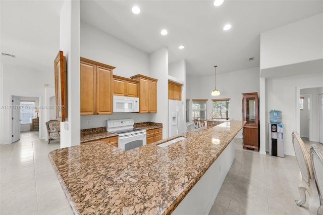 kitchen with a large island, a high ceiling, stone countertops, white appliances, and decorative light fixtures