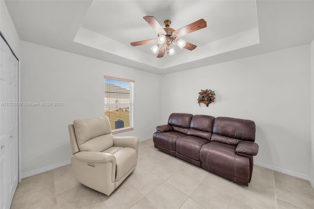 tiled living room featuring ceiling fan and a tray ceiling