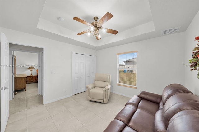 living area featuring ceiling fan, light tile patterned flooring, and a raised ceiling