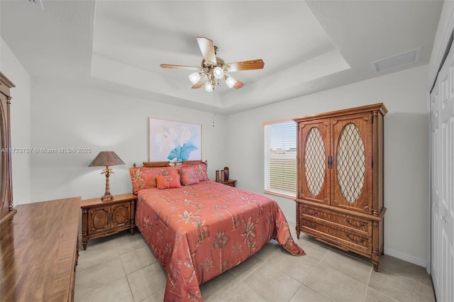 bedroom with a raised ceiling, ceiling fan, a closet, and light tile patterned floors