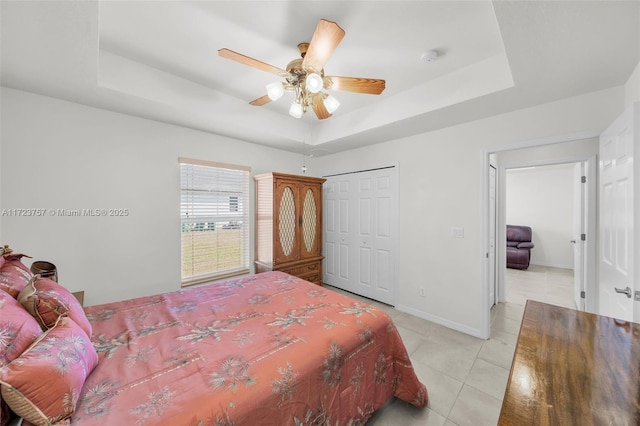 bedroom with a tray ceiling, ceiling fan, a closet, and light tile patterned floors