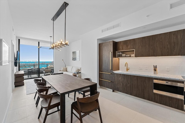 tiled dining area featuring a water view, a wall of windows, and a chandelier