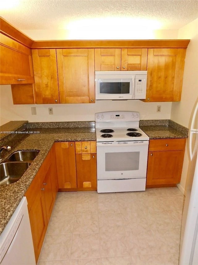 kitchen featuring sink, a textured ceiling, white appliances, and dark stone countertops