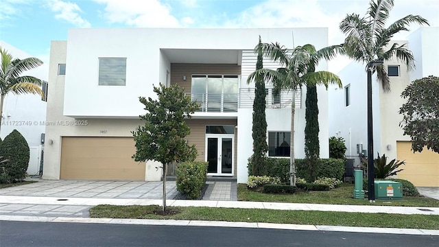 view of front of house with an attached garage, a balcony, french doors, decorative driveway, and stucco siding