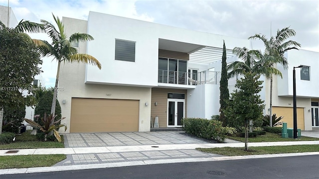 view of front of property featuring a garage, a balcony, decorative driveway, french doors, and stucco siding