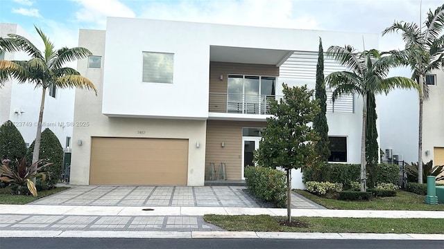 view of front of home featuring a garage, decorative driveway, a balcony, and stucco siding