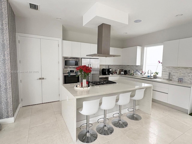 kitchen with visible vents, island range hood, a breakfast bar area, a center island, and stainless steel appliances