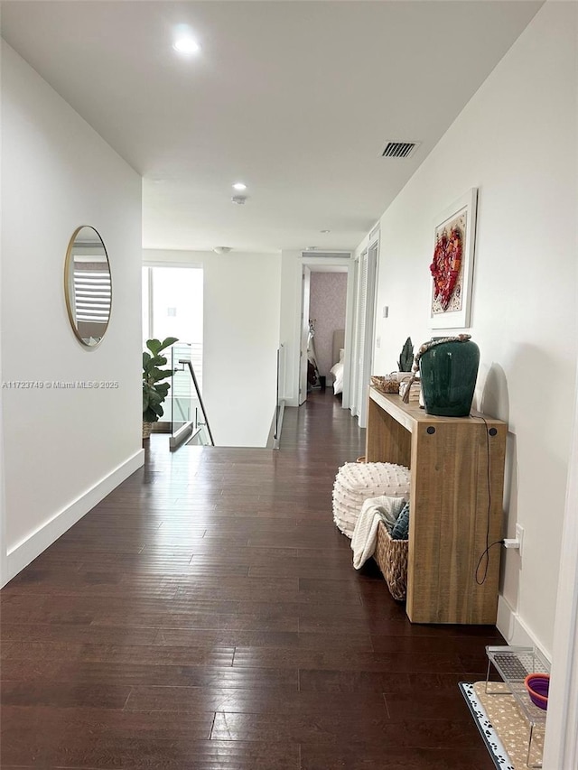 corridor featuring hardwood / wood-style flooring, an upstairs landing, visible vents, and baseboards