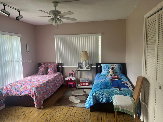 bedroom featuring ceiling fan, track lighting, a textured ceiling, a closet, and hardwood / wood-style flooring