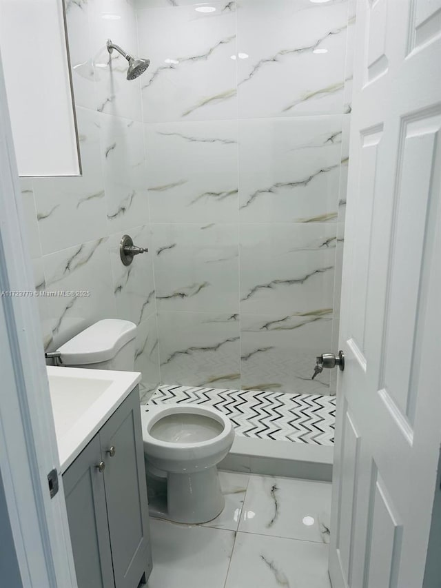 bathroom with a tile shower, vanity, and toilet