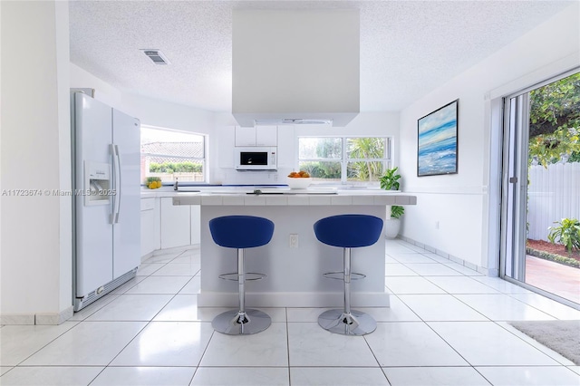 kitchen featuring white appliances, a kitchen breakfast bar, light tile patterned floors, a healthy amount of sunlight, and white cabinetry