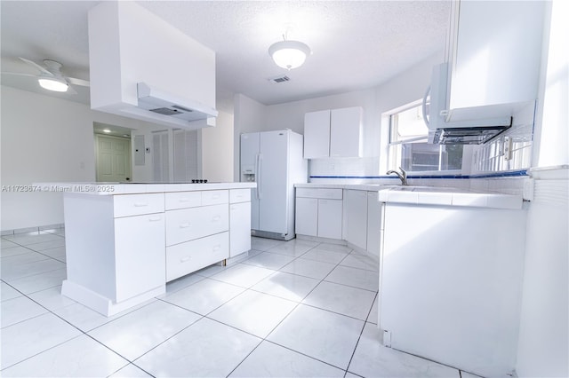 kitchen featuring white cabinets, ceiling fan, white fridge with ice dispenser, and a textured ceiling