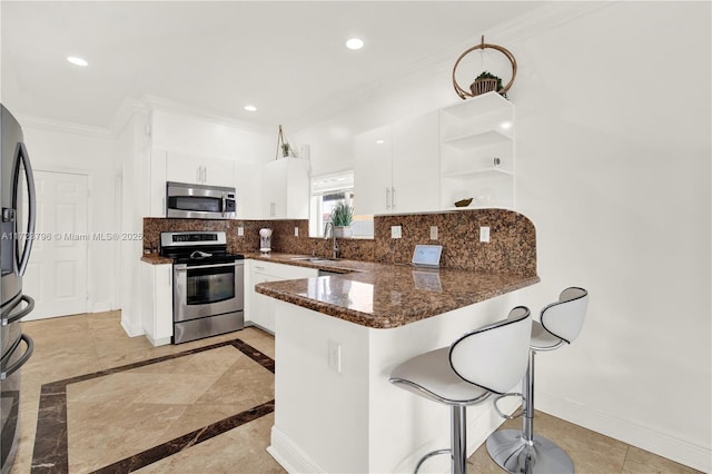 kitchen with appliances with stainless steel finishes, white cabinetry, dark stone counters, sink, and kitchen peninsula