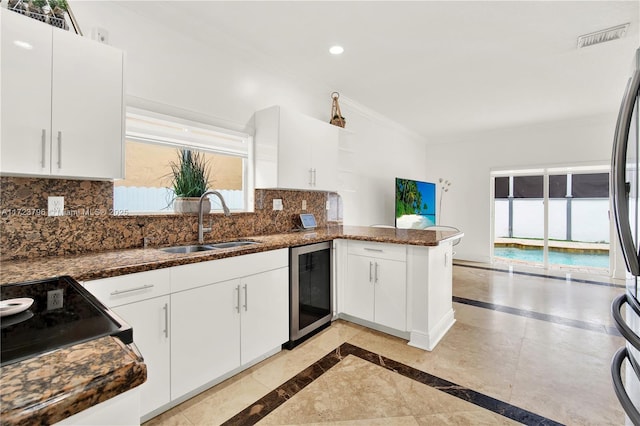 kitchen with white cabinetry, dark stone counters, wine cooler, sink, and kitchen peninsula