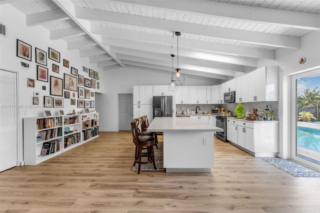 kitchen with tasteful backsplash, appliances with stainless steel finishes, a kitchen island, pendant lighting, and white cabinets