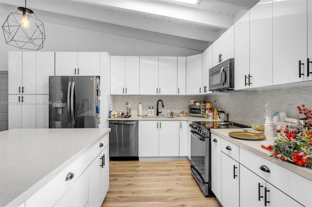 kitchen featuring white cabinetry, decorative light fixtures, lofted ceiling with beams, and stainless steel appliances