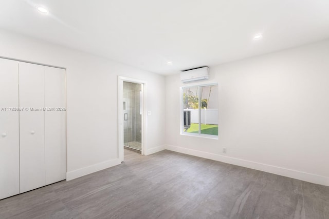 unfurnished bedroom featuring ensuite bathroom, a wall mounted AC, a closet, and light hardwood / wood-style flooring