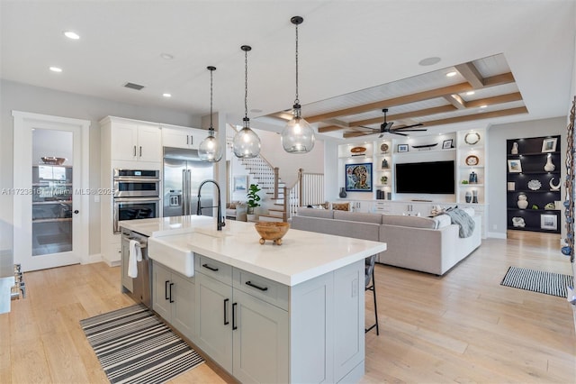 kitchen featuring appliances with stainless steel finishes, beamed ceiling, sink, a kitchen breakfast bar, and a center island with sink