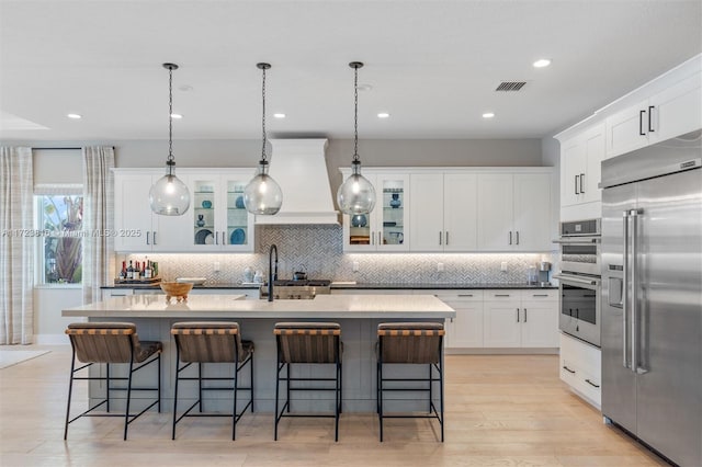 kitchen with decorative backsplash, white cabinetry, stainless steel appliances, and an island with sink