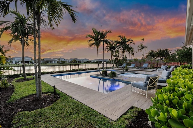 pool at dusk with a water view and a patio area