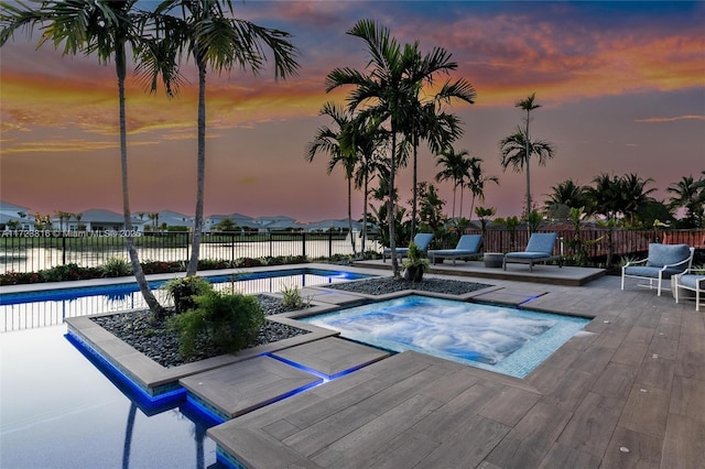 pool at dusk featuring a water view, a patio area, and an in ground hot tub