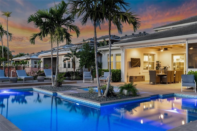 pool at dusk with ceiling fan and a patio