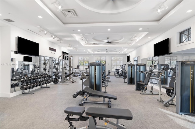 exercise room with ceiling fan, light colored carpet, and a tray ceiling