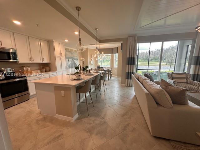 kitchen with an island with sink, a breakfast bar area, appliances with stainless steel finishes, hanging light fixtures, and white cabinets