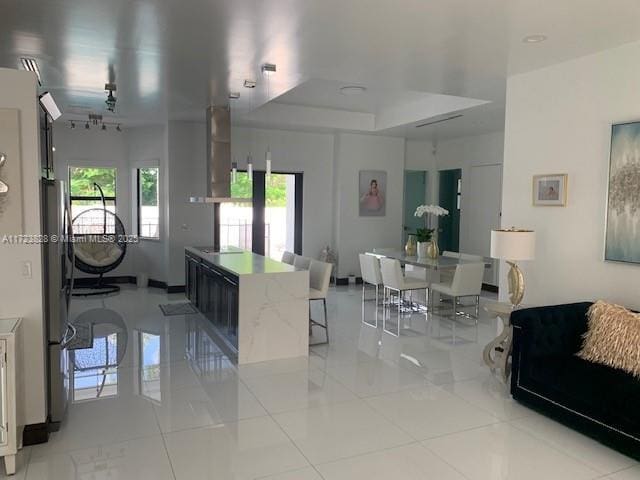 kitchen with a center island, ventilation hood, a raised ceiling, light tile patterned floors, and black electric cooktop