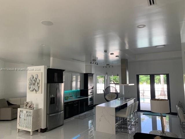 kitchen with french doors, wall chimney exhaust hood, stainless steel fridge, black electric cooktop, and a kitchen island