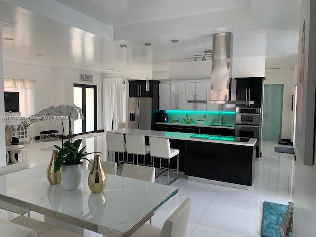 kitchen with stainless steel appliances, sink, wall chimney range hood, a center island, and white cabinetry