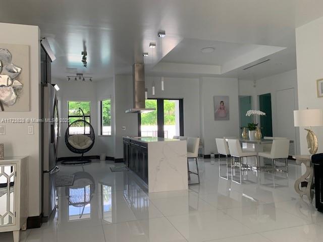 kitchen featuring a raised ceiling, stainless steel refrigerator, light tile patterned floors, and wall chimney range hood