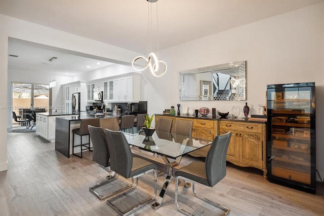 dining room with light wood-type flooring, an inviting chandelier, and wine cooler