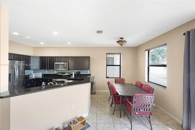 kitchen featuring a breakfast bar area, tasteful backsplash, light tile patterned floors, dark stone countertops, and appliances with stainless steel finishes