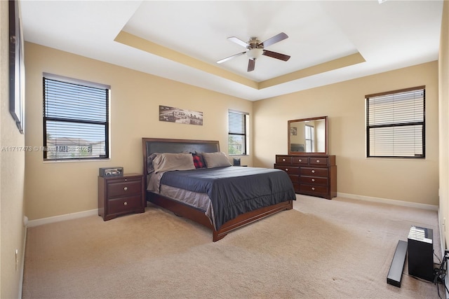 bedroom featuring ceiling fan, a tray ceiling, and light carpet