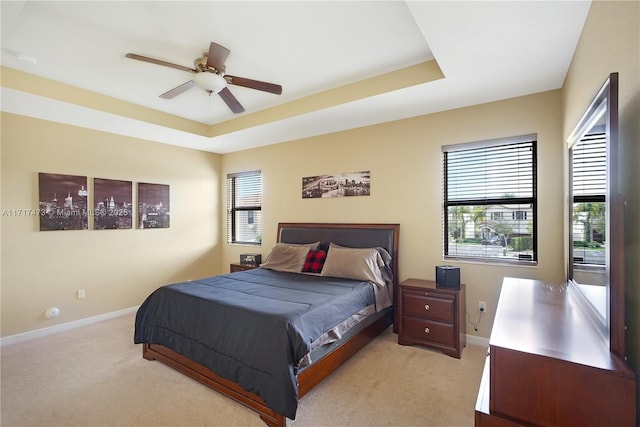 bedroom featuring light carpet, a tray ceiling, and ceiling fan