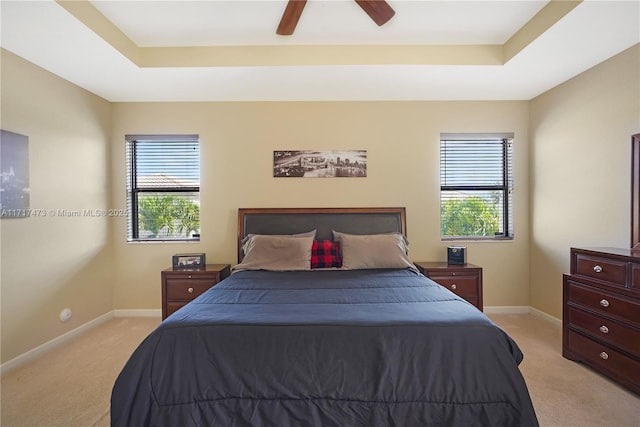 carpeted bedroom with multiple windows, ceiling fan, and a tray ceiling