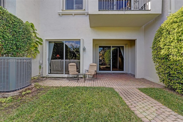 property entrance with cooling unit, a balcony, a yard, and a patio area