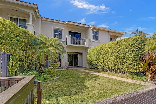 rear view of property featuring a balcony and a lawn