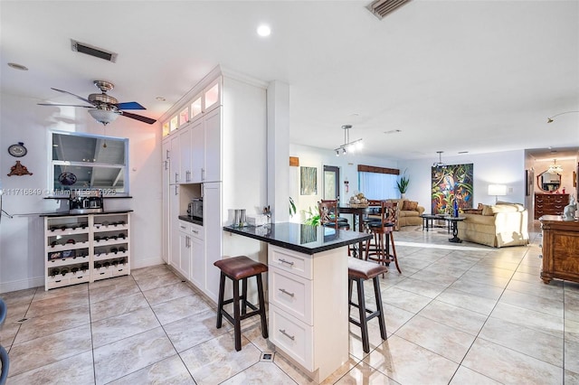 kitchen featuring a kitchen bar, ceiling fan, pendant lighting, light tile patterned floors, and white cabinetry