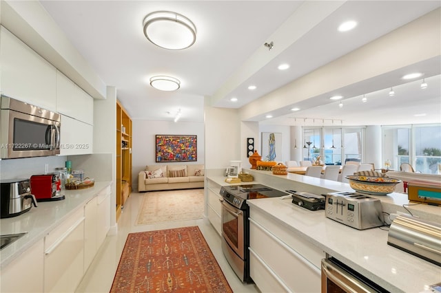 kitchen with appliances with stainless steel finishes, light tile patterned floors, white cabinetry, and light stone counters