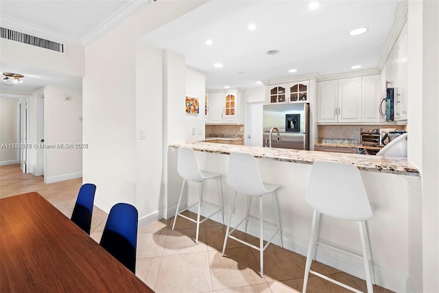 kitchen featuring white cabinetry, stainless steel refrigerator with ice dispenser, backsplash, light tile patterned floors, and ornamental molding