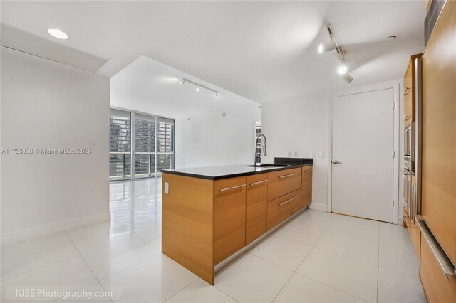 kitchen with kitchen peninsula, sink, light tile patterned floors, a wall of windows, and rail lighting