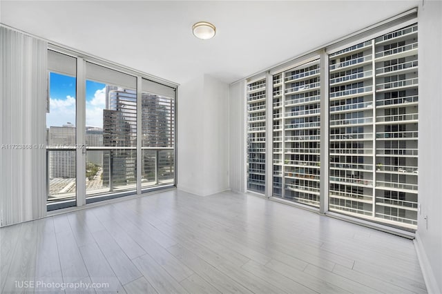 unfurnished room featuring a view of city, wood finished floors, and floor to ceiling windows